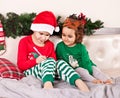 Funny boy kid in Santa hat and girl in deer mask writing letter to Santa Claus sitting on a bed