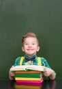 Funny boy reading a book near empty green chalkboard