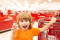 Funny boy with shopping cart full of fresh organic vegetables and fruits standing in grocery department of food store or Royalty Free Stock Photo