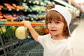 Funny boy with shopping cart full of fresh organic vegetables and fruits standing in grocery department of food store or Royalty Free Stock Photo