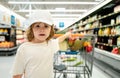 Funny boy with shopping cart full of fresh organic vegetables and fruits standing in grocery department of food store or Royalty Free Stock Photo