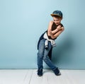 Naughty schoolboy in stylish cap jumping in place looking down under his feet with roguish smile. isolated on blue background Royalty Free Stock Photo