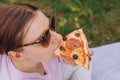 Funny brunette girl in sunglasses eating pizza on nature background. Attractive girl feels hungry and loves the taste