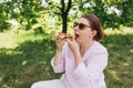 Funny brunette girl in sunglasses eating pizza on nature background. Attractive girl feels hungry and loves the taste