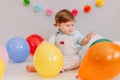 Funny Caucasian baby boy celebrating first birthday. Child kid toddler sitting on floor with colorful balloons. Celebration of Royalty Free Stock Photo