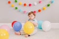 Funny Caucasian baby boy celebrating first birthday. Child kid toddler sitting on floor with colorful balloons. Celebration of Royalty Free Stock Photo