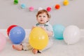 Funny Caucasian baby boy celebrating his first birthday. Child kid toddler sitting on floor with colorful balloons. Celebration of Royalty Free Stock Photo