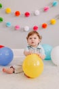 Funny Caucasian baby boy celebrating his first birthday. Child kid toddler sitting on floor with colorful balloons. Celebration of Royalty Free Stock Photo