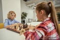 Funny caucasian boy looking emotional while playing chess with his friend, sitting at the table in school Royalty Free Stock Photo