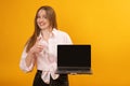 Funny caucasian woman holding laptop computer and shows thumbs up looking at the camera on yellow background. Copy space, mock up Royalty Free Stock Photo