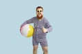 Funny cheerful chubby guy holds inflatable ball and shows thumb up on pastel turquoise background.
