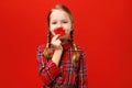 Funny cheerful little girl makes artificial fake lips on a red background. Child fooling around