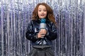 Funny cheerful stylish girl with a microphone in her hands on a shiny tinsel background