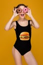 Funny cheerful woman in swimsuit holding donuts against her eyes