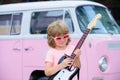 Funny child with blonde curly hair playing guitar on pink background. Kids music school. Royalty Free Stock Photo