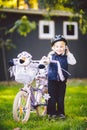 Funny child Caucasian girl blonde in a bicycle helmet near a purple bike with a basket in outside the park on a green Royalty Free Stock Photo