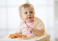 Funny child eating noodle. Grimy kid eats spaghetti with fork sitting on table at home