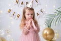 Funny child girl in pink dress and birthday hat blowing in whistle and celebrating her birthday Royalty Free Stock Photo