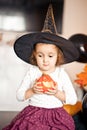 funny child girl in witch costume for Halloween holding a pumpkin lantrern