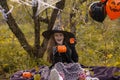 Funny child girl in a witch costume for Halloween holds a mug in the form of a pumpkin.