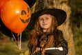 Funny child girl in a witch costume for Halloween with a small dog and with black and orange balloons. Royalty Free Stock Photo