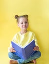 Funny child girl yellow jacket on a yellow background, sitting, reading a book, development and school concept Royalty Free Stock Photo