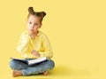 Funny child girl yellow jacket on a yellow background, sitting, reading a book, development and school concept Royalty Free Stock Photo