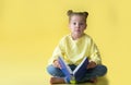 Funny child girl yellow jacket on a yellow background, sitting, reading a book, development and school concept Royalty Free Stock Photo