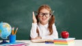 Funny child   schoolgirl    student  raises his hand up near school blackboard Royalty Free Stock Photo