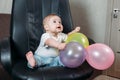 Funny child sitting on chair little boy having fun playing big colored balloons Royalty Free Stock Photo