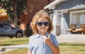 Funny child in sunglasses with thumbs up sign close up. Kids outdoor home, near house, head portrait.