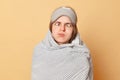 Funny childish woman wrapped blanket and wearing sleeping eye mask isolated over beige background standing with crossed eyes and Royalty Free Stock Photo