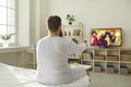 Funny chubby guy in pajamas sitting in bedroom and watching TV show on television