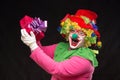 Funny clown with hair and a cheerful make-up holding a gift