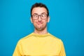 Funny comic man in glasses makes grimace with crosses eyes. Young man in yellow t-shirt with crazy expression has fun alone