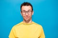 Funny comic man in glasses makes grimace with crosses eyes. Young man in yellow t-shirt with crazy expression has fun alone