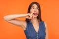 Funny comical brunette woman in denim dress picking nose and showing tongue with humorous stupid expression