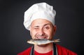 Funny cook in a hat with a dry fish in his teeth.