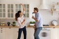 Playful young couple prepare food at kitchen enjoy singing songs