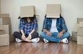 Funny couple move with empty cardboard boxes on their heads sitting on floor after at new home Royalty Free Stock Photo