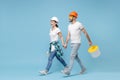 Funny couple woman man in helmet hardhat glasses hold paint bucket, paint roller isolated on blue background