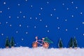 Funny cozy scene with Christmas toys on classic blue. Christmas tree is moved home by bicycle on the snow road with