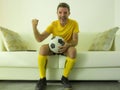 Funny and crazy soccer fan man dressed in his team uniform watching football game on television celebrating scoring goal excited