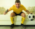 Funny and crazy soccer fan man dressed in his team uniform watching football game on television celebrating scoring goal excited