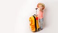 Funny curly little baby girl in a hat, T-shirt and jeans with a yellow suitcase is smiling on a white background waiting for an Royalty Free Stock Photo