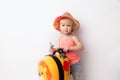 Funny curly little baby girl in a hat, T-shirt and jeans with a yellow suitcase is smiling on a white background waiting for an Royalty Free Stock Photo