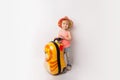 Funny curly little baby girl in a hat, T-shirt and jeans with a yellow suitcase is smiling on a white background waiting for an Royalty Free Stock Photo