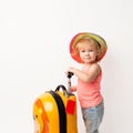 Funny curly little baby girl in a hat, T-shirt and jeans with a yellow suitcase is smiling on a white background waiting for an Royalty Free Stock Photo