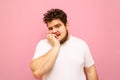 Funny curly overweight young man stands on a pink background and bites his nails with emotion. Fat stressful guy tense isolated on