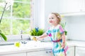 Funny curly toddler girl in colorful dress washing dishes